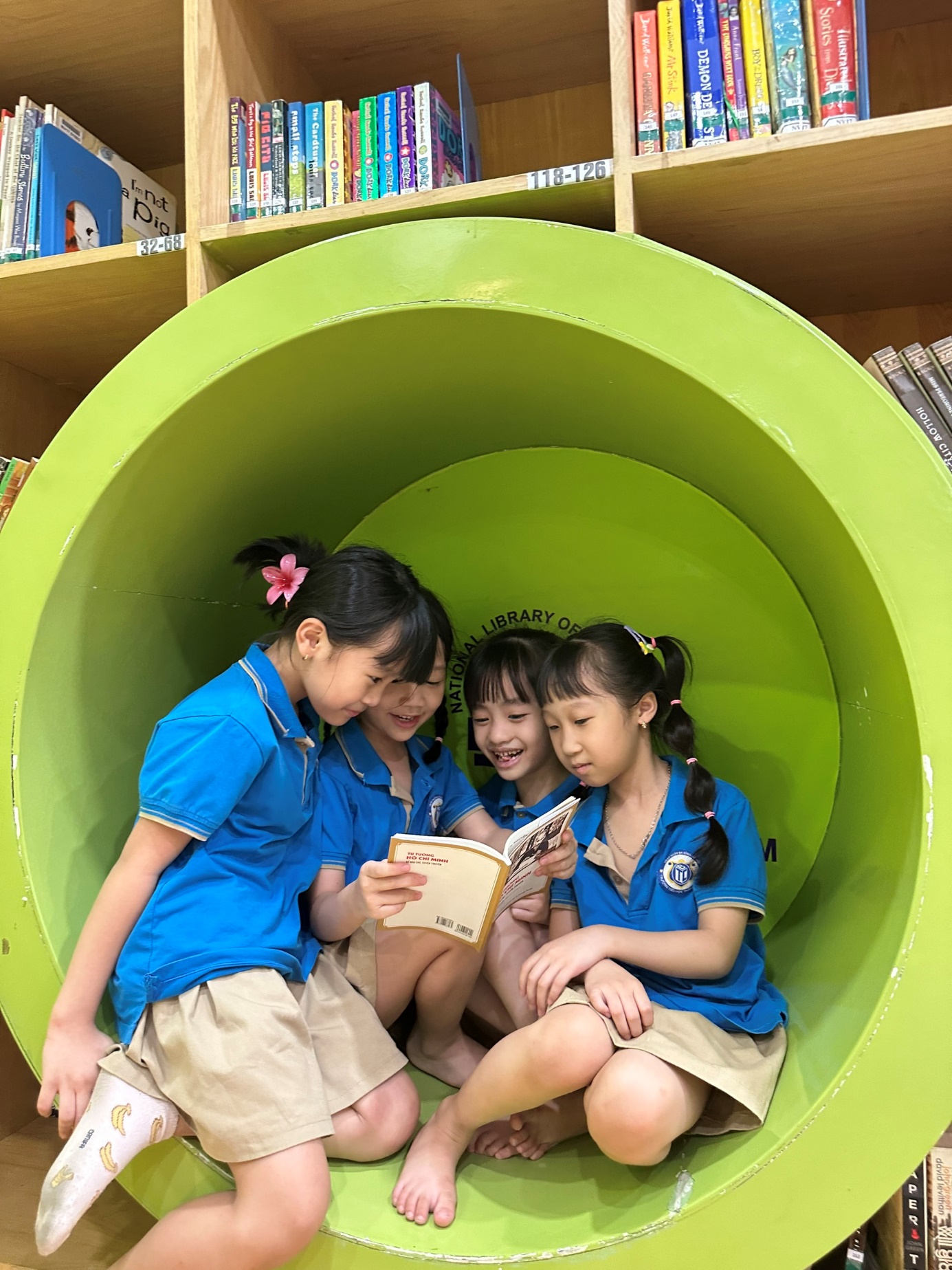A group of girls sitting on a green tube reading a book

Description automatically generated