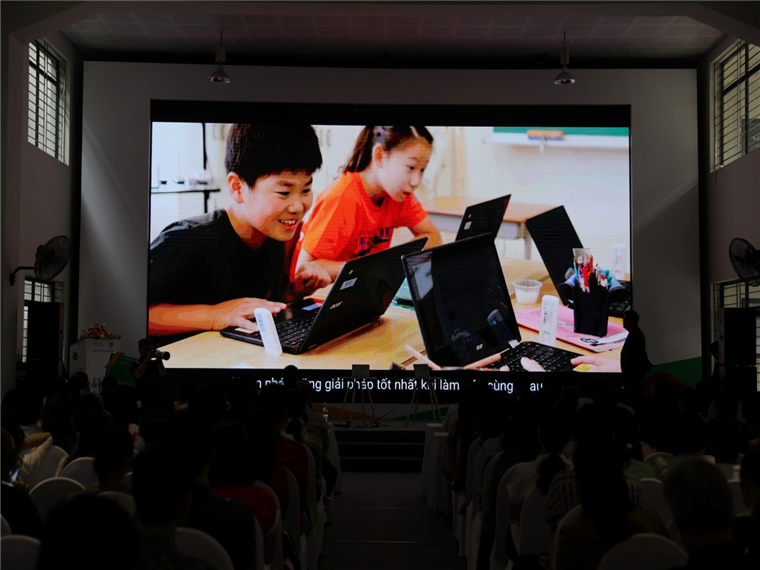 A large screen showing a group of kids using laptops

Description automatically generated
